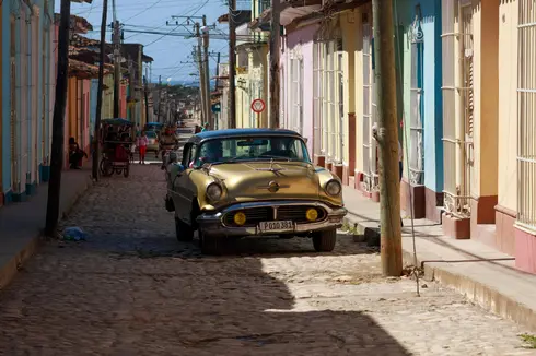 Oldsmobile dorata degli anni '50 percorre una strada in pavé di Trinidad, Cuba, tra case color pastello — simbolo di adattamento, durata e Frankenstein meccanico